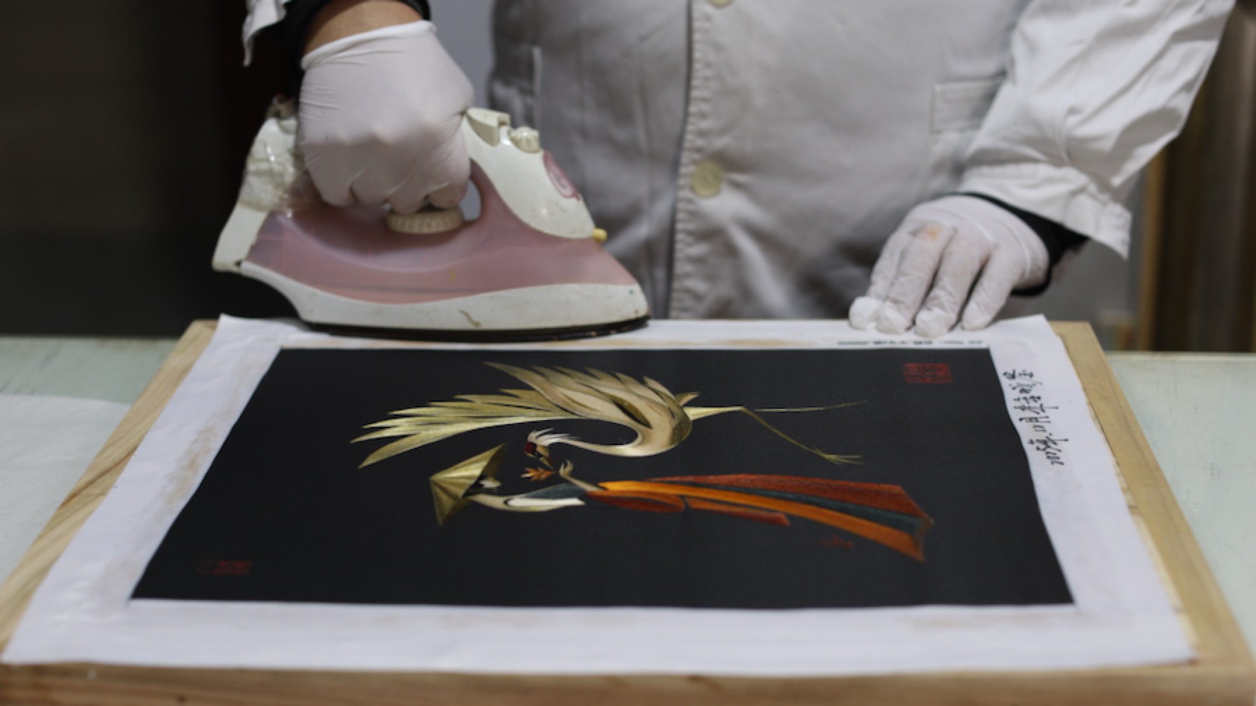 A white-gloved studio practitioner pressing the Crane Dance silk embroidery.
